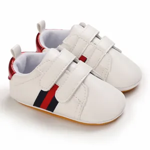 Close-up of white baby walker shoes with red and navy side stripes and soft rubber soles