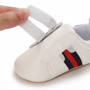 Close-up view of white baby walker shoe featuring velcro straps and navy red stripes.