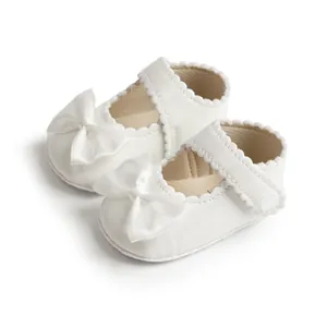 Chaussures de princesse blanches pour bébé avec nœud en satin et bord festonné.