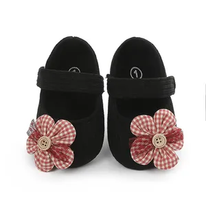 Vista detallada de zapatos de bebé negros con flor de cuadros rojos y botón central.