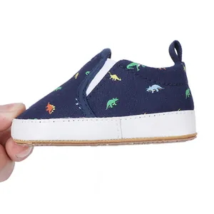 Detail of navy blue baby slip-on shoe featuring colorful dinosaur print and white sole.
