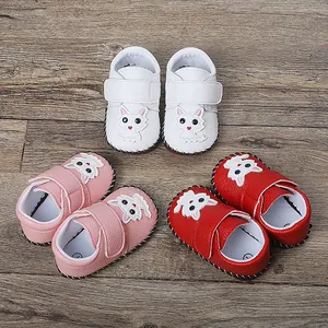 Detailansicht von weißen, rosa und roten Cartoon-Katzen-Babyschuhen auf Holzgrundlage