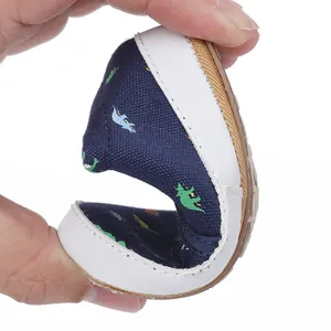 Flexible baby walking shoe with dinosaur print shown bent to demonstrate its softness.