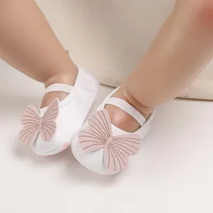 Detail of white baby walking shoes with pink butterfly decoration and soft fabric sole