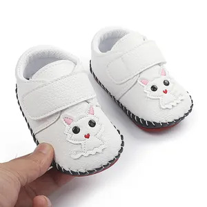 Nahaufnahme weißer Babylauflernschuhe mit süßer Katze und robuster, roter Gummisohle