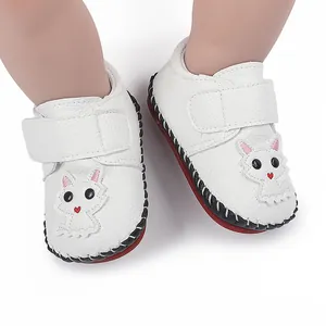 Detailaufnahme weißer Babylauflernschuhe mit Cartoon-Katze und roter Sohle