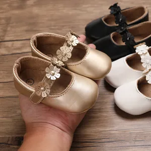 Detailansicht von goldenen Baby Prinzessinnen-Lauflernschuhen mit Blumenriemen in der Hand