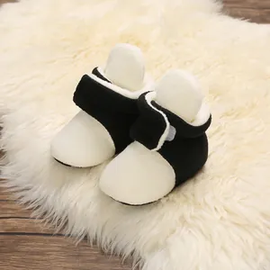 Close-up view of soft black and white plush baby winter boots on a cozy white fluffy rug