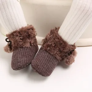 Close-up detail of brown infant winter booties with plush faux fur trim and cute pom-poms