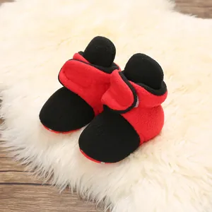 Red and black fleece baby winter booties with soft soles on a white plush rug.