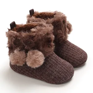 Macro view of brown infant winter boots featuring soft faux fur and pom-poms