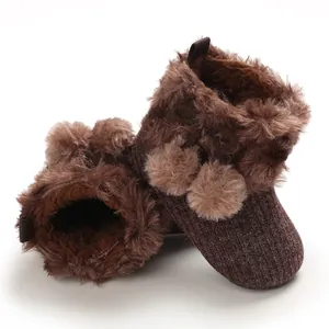 Detailed view of brown baby winter boots with plush faux fur lining and pom-poms
