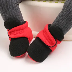 Detailed macro view of red and black baby fleece booties with soft soles and velcro straps.