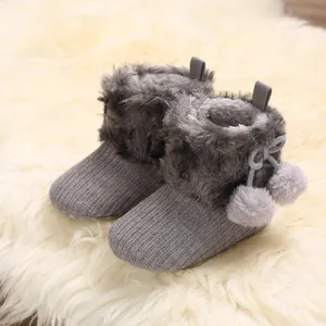 Close-up view of grey knit baby booties featuring soft faux fur trim and pom-pom detail