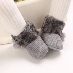 Close-up view of grey knit baby girl booties featuring soft faux fur trim and cute pom-poms