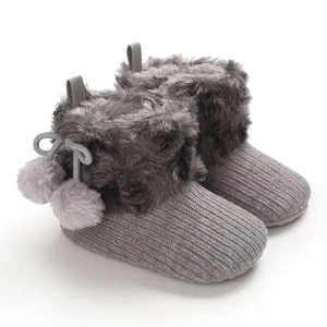 Close-up of adorable grey knitted baby booties with faux fur trim and cute pom-poms