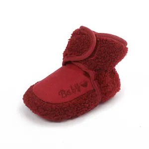 Close-up detail of warm red plush baby bootie with 'Baby' heart embroidery and velcro