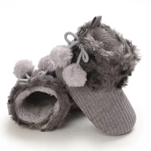 Close-up of adorable gray knit baby girl shoes with plush faux fur and cute pom-poms.