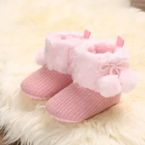 Close-up of cute pink knitted baby boots featuring soft faux fur and pom-pom detail