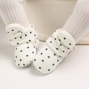 Primer plano de botas de nieve blancas para bebé con estrellas sobre leggings acanalados.