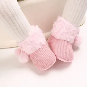 Detailed macro view of cute pink baby girl knitted booties featuring soft pom-poms and rose fur