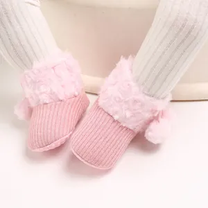 Close-up of pink knitted baby shoes with fluffy faux fur trim and pom-poms