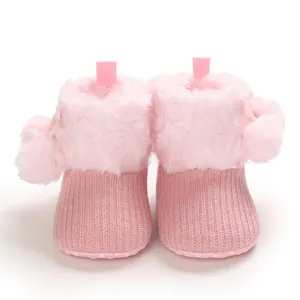 Close-up detail of cute pink knitted baby booties with soft faux fur and fluffy pom-poms