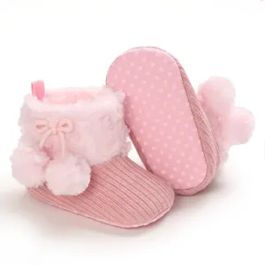 Detailed view of pink knitted baby boots with fluffy pom-poms and non-slip sole