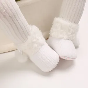 Detailed macro shot of white knitted infant boots with soft faux fur and cute pom-poms