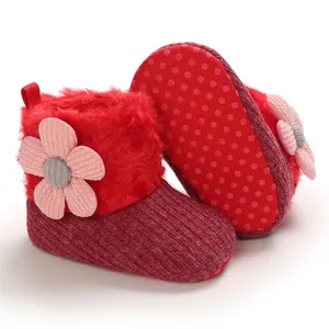 Close-up of red baby winter snow boots with plush fur and pink flower decoration.