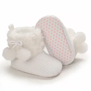 Close-up view of white knitted baby booties with soft faux fur trim and pom-pom details