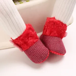 Close-up of red plush baby boots with soft ribbed knit and pink bow detail.