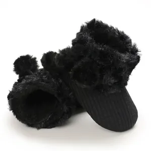 Macro view of black knitted baby booties featuring soft faux fur and cute pom-poms detail