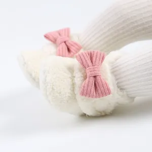 Detailaufnahme von weichen weißen Fleece-Babyschuhen mit einer süßen rosa gestrickten Schleife