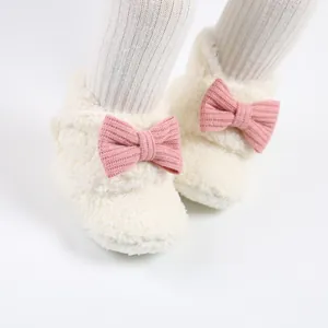 Nahaufnahme von weichen weißen Plüsch-Baby-Winterstiefeln mit rosa Strickschleife