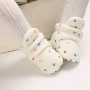 Close-up of cream fleece baby booties with colorful heart patterns and soft soles