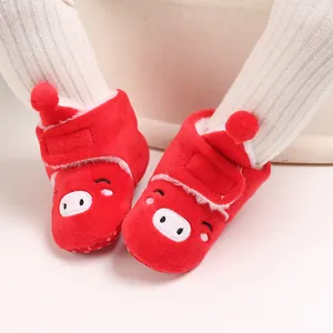 Gros plan de bottes de neige rouges en peluche pour bébé avec motif cochon et doublure douce.