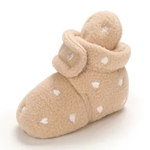 Dettaglio ravvicinato di scarpine da neonato in peluche beige con motivo a cuori