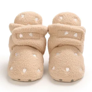Close-up of beige fleece baby boots with embroidered white heart pattern and velcro straps.