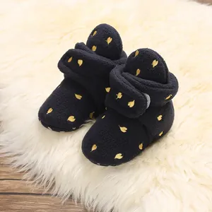 Close-up of navy fleece baby booties with yellow embroidered hearts on a white fur rug.