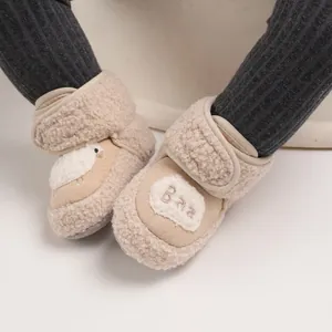 Dettaglio di scarpine per neonati in pile beige con ricamo 'Baa' e consistenza morbida.
