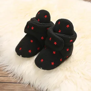 Close-up of soft black baby booties with red star embroidery on a plush white rug