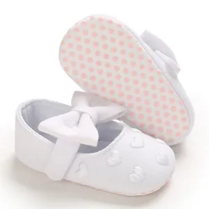 Nahaufnahme von weißen Baby-Prinzessinenschuhen mit Schleife und Herz-Stickerei-Details
