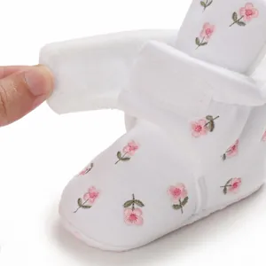 Nahaufnahme weißer Baby-Winterstiefel mit Blumenstickerei und Klettverschluss.