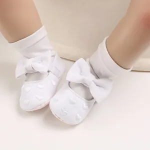 Nahaufnahme weißer Babylauflernschuhe mit eleganter Schleife und Herzstickerei