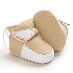 Detailaufnahme von Baby-Schneeschuhen mit weißen Engelsflügeln auf khakifarbenem Stoff