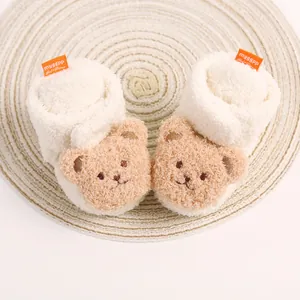 Detailaufnahme weicher weißer Babyschuhe mit einem niedlichen braunen Plüsch-Teddybär-Gesicht