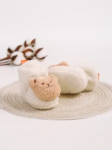 Nahaufnahme von weißen, flauschigen Babyschuhen mit süßem Bärengesicht auf Strohmatte