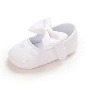 Detailansicht weißer Baby-Prinzessinenschuhe mit großer Schleife und Herzstickerei.