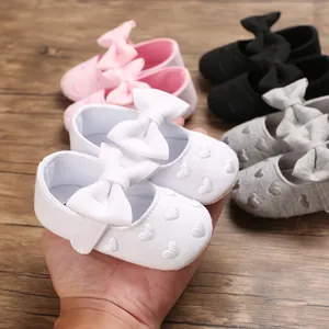 Detailansicht weißer Baby-Prinzessinnenschuhe mit großer Schleife und Herzstickerei